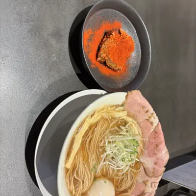 Bowl of clear ramen with pork next to a dish of chili powder