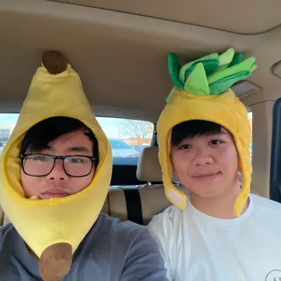 Two friends taking a car selfie in banana and pineapple hats