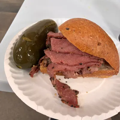 Pastrami sandwich on a paper plate with a pickle