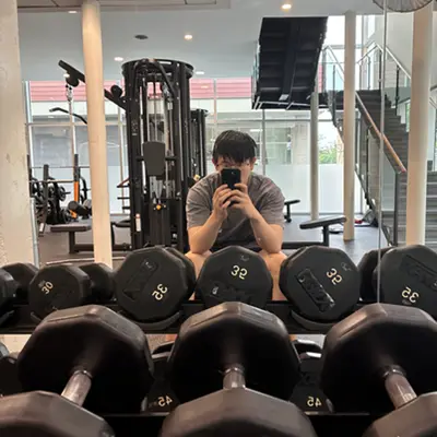 Gym mirror selfie behind a rack of dumbbells