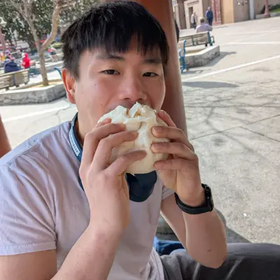 Joseph biting into a large steamed bun outdoors