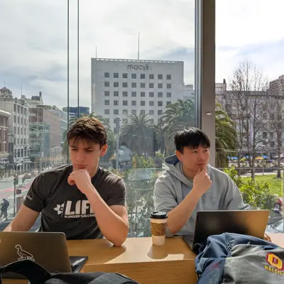 Two friends with laptops by a window overlooking Union Square