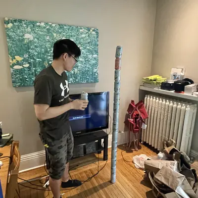 Man holding a drink beside a tall wrapped tube in a living room