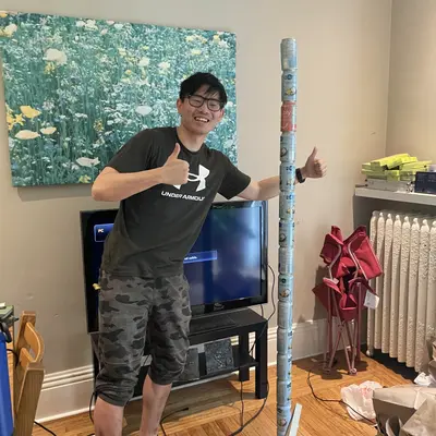 Joseph giving thumbs up next to a tall wrapped tube in a living room