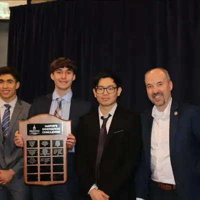 Four people in suits holding a Mayor's Innovation Challenge plaque