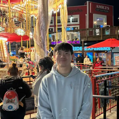 Joseph in a light hoodie at a nighttime pier with a carousel
